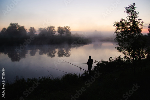 Lonely fisherman angling at a lake in the early morning just before sunrise