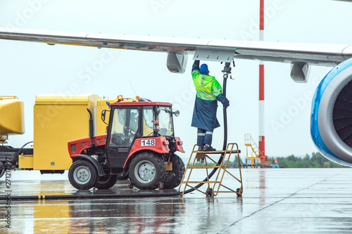 Aircraft refueling at the airport. Fuel tank and tractor on the background.
