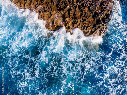 Top view Azure blue sea with waves beating on beach and rocks. Aerial photo.
