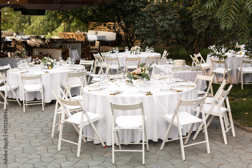 Wedding table setting decorated with fresh flowers in a brass vase. Wedding floristry. Banquet table for guests outdoors with a view of green nature. Bouquet with roses, eustoma and eucalyptus leaves