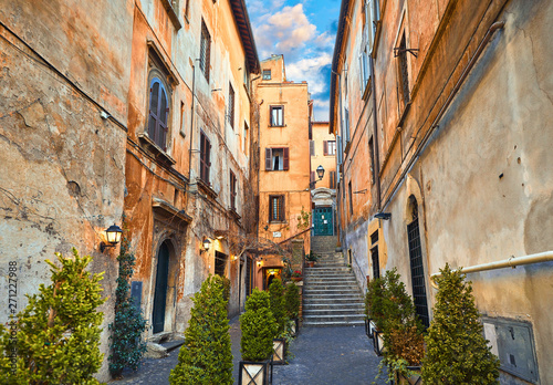 Fototapeta Naklejka Na Ścianę i Meble -  Rome, Italy. Yard of old street in downtown with antique building and stone stairs. Evening cityscape with street lamps on walls and decorative plants in flowerpots.