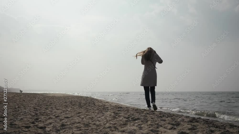 young woman in a raincoat dancing on the beach of the sea, walking along the coast young woman in a raincoat dancing on the beach of the sea, walking along the coast