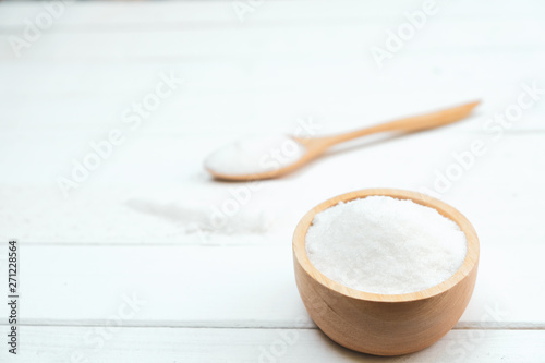 Sugar is in a wooden bowl on a white table.