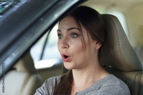 Young attractive caucasian woman behind the wheel driving a car with grimace of astonishment or shock, mouth opened. Strong emotions, wow expression. Copy space. © Elena