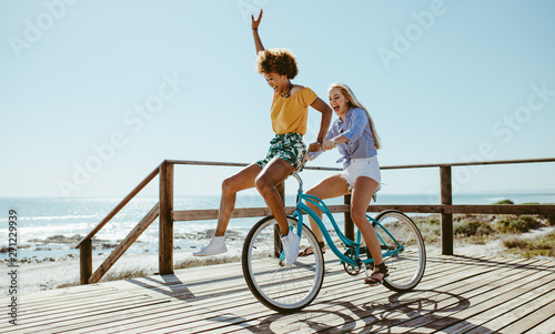 Female friends having fun on a bike at beach