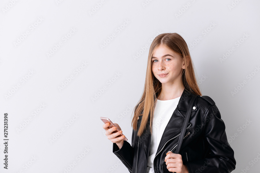 Stylish teenage girl with mobile phone on light background