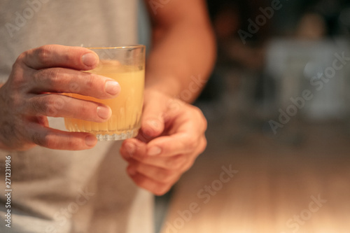 Vegan lifestyle. Cropped shot of man standing in kitchen with glass of fresh natural orange juice. Dark blur background.