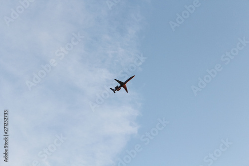 Fototapeta Naklejka Na Ścianę i Meble -  Red plane on cloudy background. Airplane flying in clear pale blue sky.