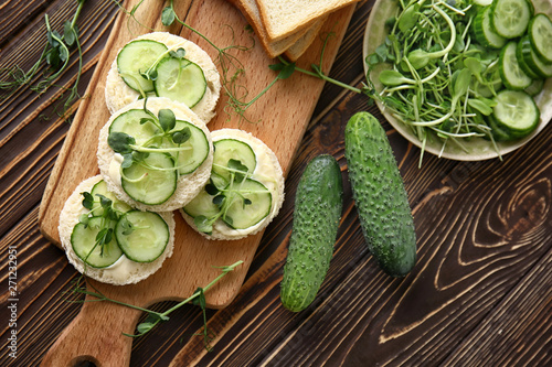 Board with tasty cucumber sandwiches on wooden table