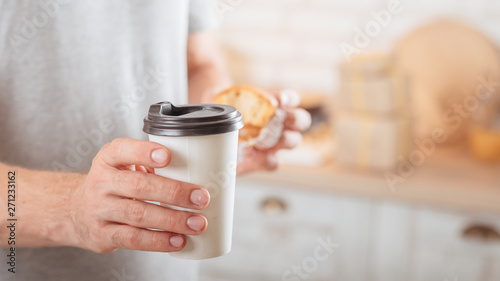 Morning habit. Closeup of disposable cup with hot drink in man hand. Blur kitchen background.
