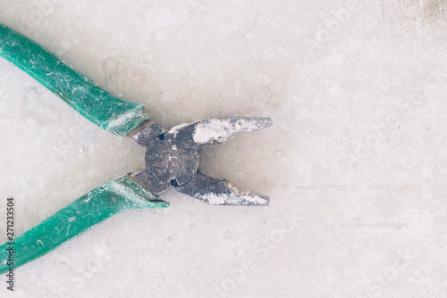 Pliers with green handle in white paint on the gray concrete background, toned. Close-up, top view, flat lay, copy space © Anna