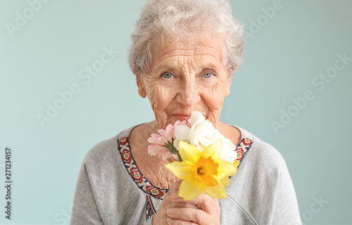 Portrait of senior woman with bouquet of flowers on grey background photo