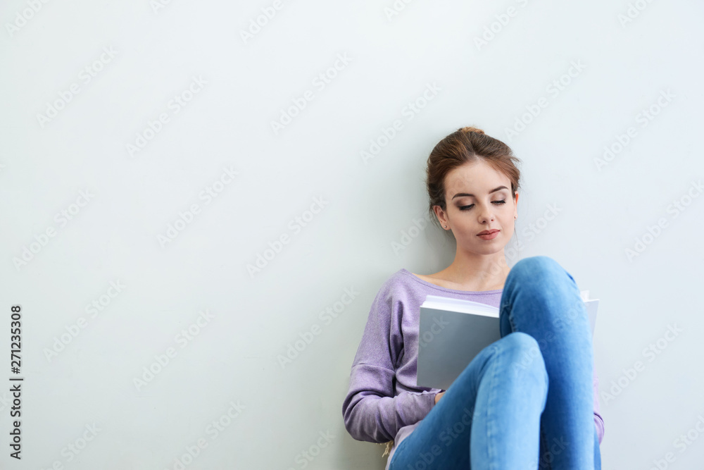 Beautiful young woman reading book near light wall Beautiful young woman reading book near light wall