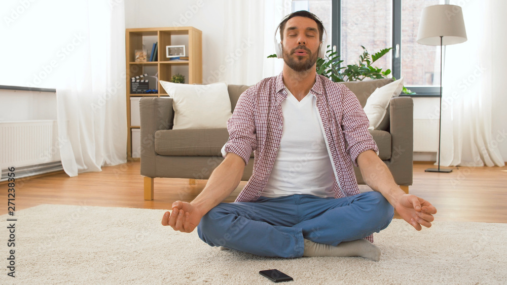 mindfulness, spirituality and music concept - man in headphones meditating in lotus pose at home mindfulness, spirituality and music concept - man in headphones meditating in lotus pose at home