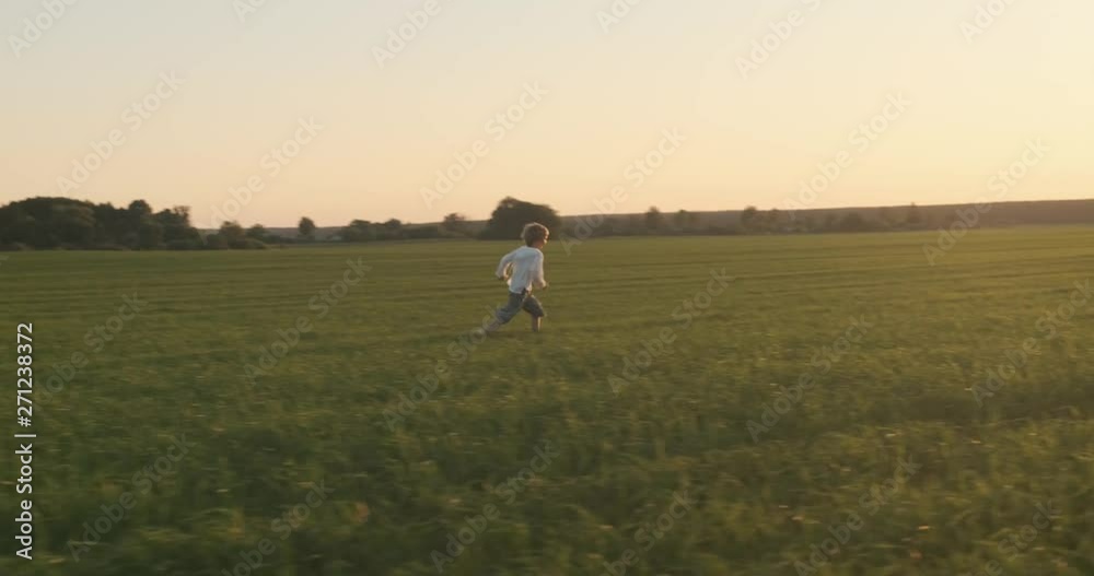 Happy child running on the meadow in the summer while sunset. Happy 7 year old cheerful boy is playing on field. Happiness concept. Active blond hair boy on nature in the spring. Slow motion Happy child running on the meadow in the summer while sunset. Happy 7 year old cheerful boy is playing on field. Happiness concept. Active blond hair boy on nature in the spring. Slow motion