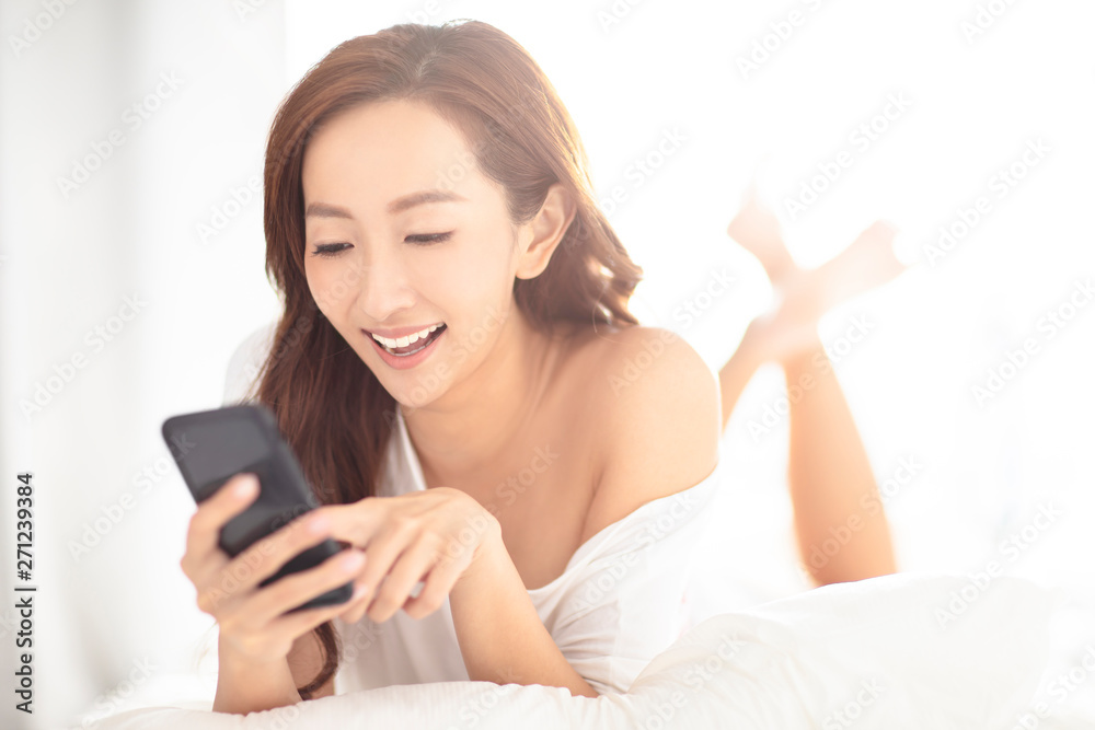 young smiling woman watching mobile phone on bed young smiling woman watching mobile phone on bed