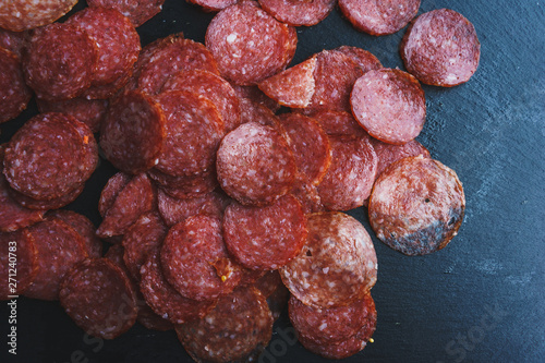 Thinly sliced sausage slices on a black stone board. 