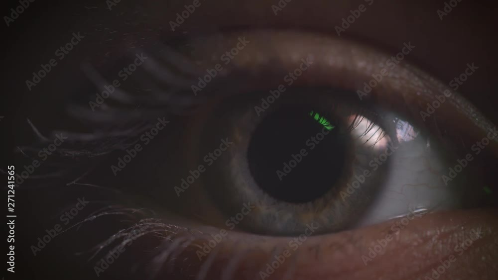 Close-up shoot of gray eye blinking with reflection of green lamp on it in complete darkness. Close-up shoot of gray eye blinking with reflection of green lamp on it in complete darkness.