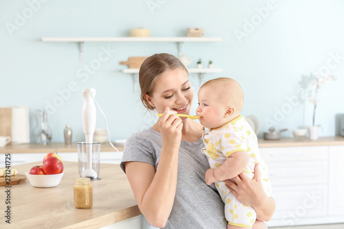 Mother feeding her little baby in kitchen at home photo