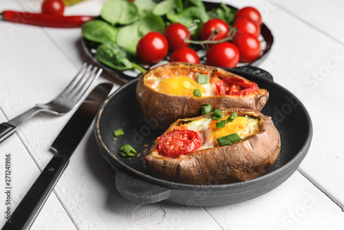 Baked sweet potato with egg and tomato on white table