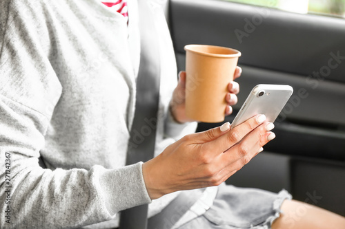 Young woman with mobile phone and coffee in car