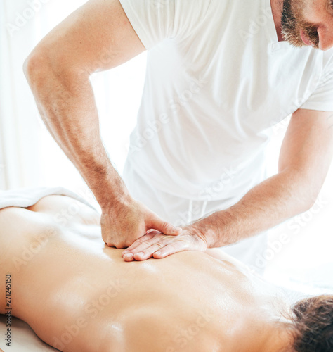 Bearded Masseur man doing massage manipulations on the Scapula area zone during young female body massaging.