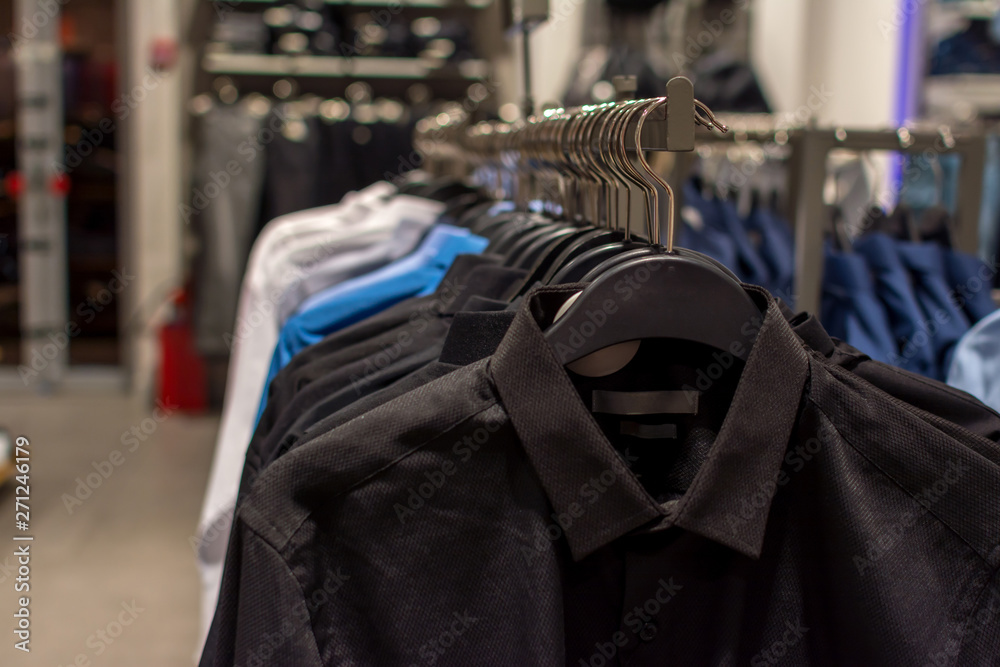 Black, blue and white men's shirts on hangers inside the store, close-up with a blurred background