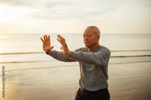 Asian Senior old man practice Tai chi and Yoga pose on the beach sunrise