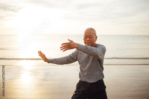 Asian Senior old man practice Tai chi and Yoga pose on the beach sunrise photo