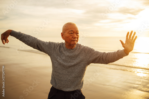 Asian Senior old man practice Tai chi and Yoga pose on the beach sunrise