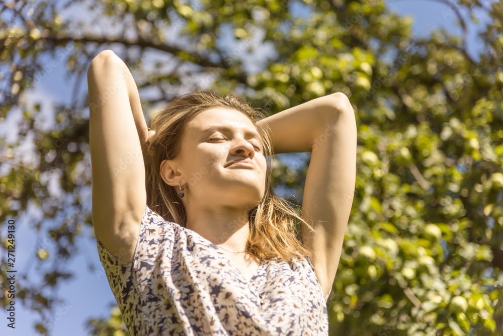 Young attractive happy woman lit by the bright sun against the background of the garden
