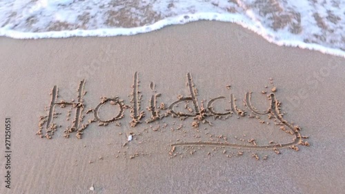 wave wipes the word holiday written in sand