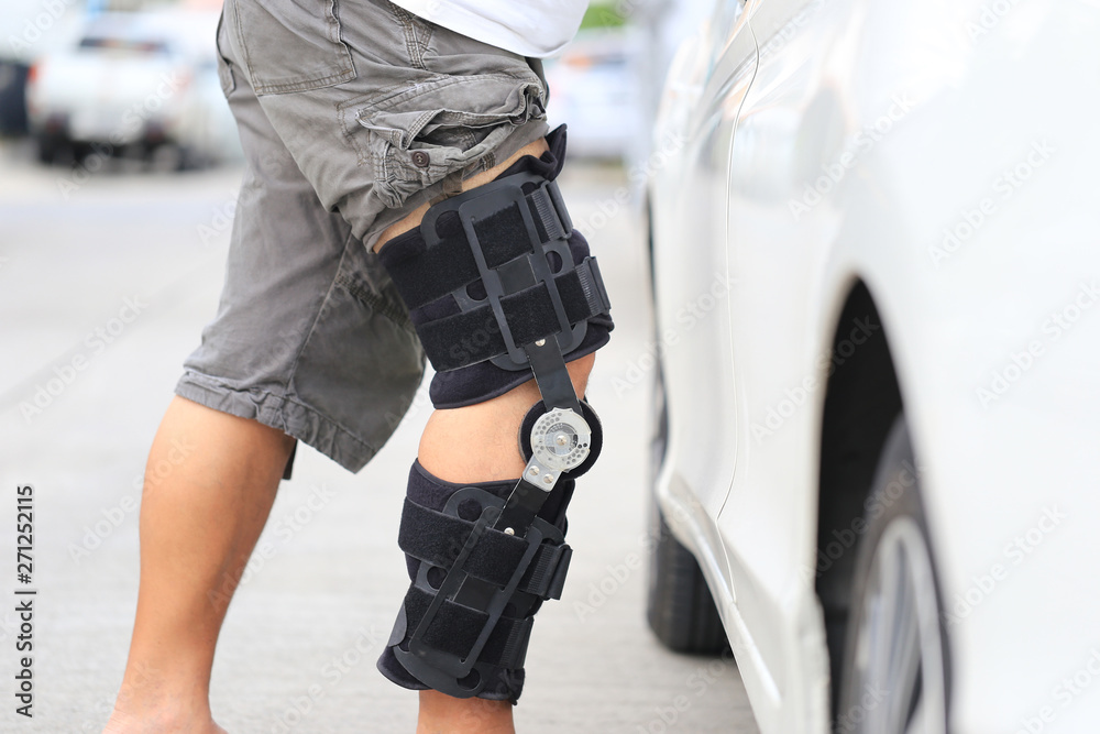 Senior man wear knee support brace on leg standing at the car parking lot, Medical and healthcare concept Senior man wear knee support brace on leg standing at the car parking lot, Medical and healthcare concept