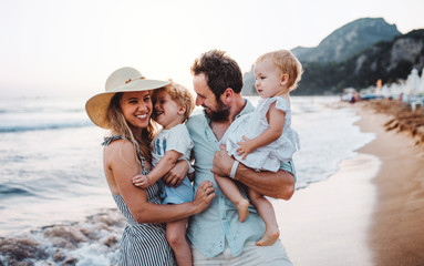 A young family with two toddler children standing on beach on summer holiday.