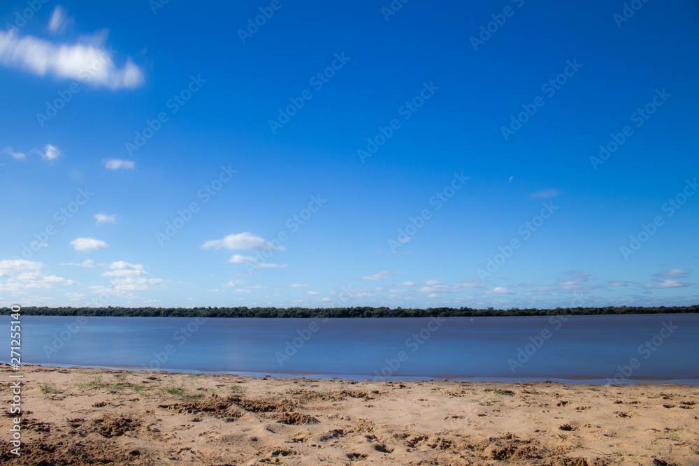 An Small beach on the edge of the river. The water moves calmly.