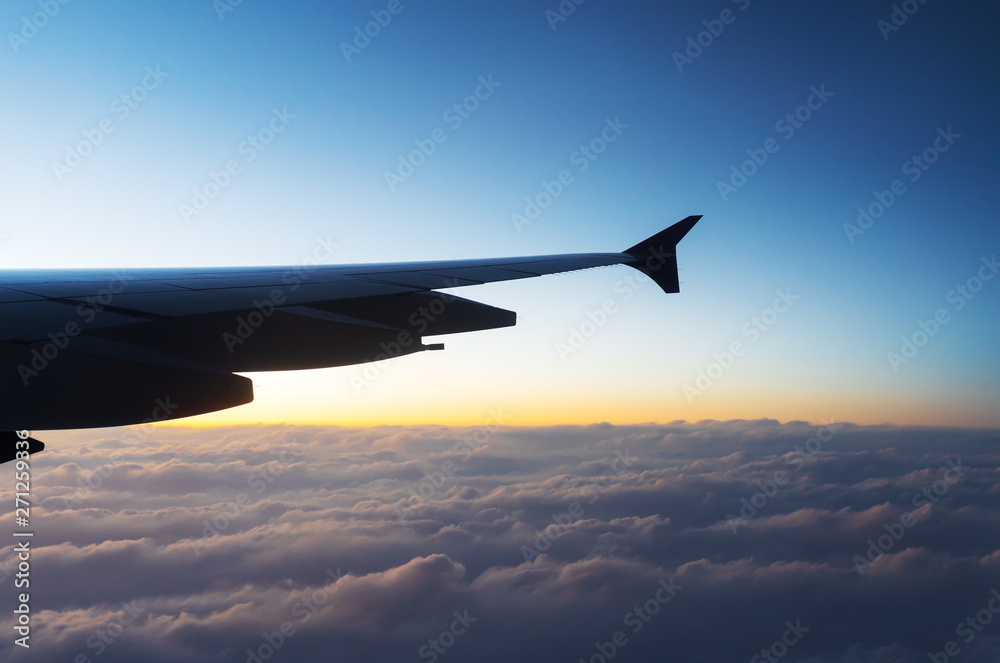 Wing of airplane flying above the clouds in sky with sunset Wing of airplane flying above the clouds in sky with sunset