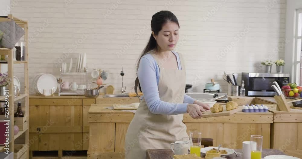 slow motion of japanese mom walking out from kitchen putting tasty homemade bread on woo plate on table talking to daughter in the morning. mother fixing little girl elementary school dress uniform slow motion of japanese mom walking out from kitchen putting tasty homemade bread on woo plate on table talking to daughter in the morning. mother fixing little girl elementary school dress uniform
