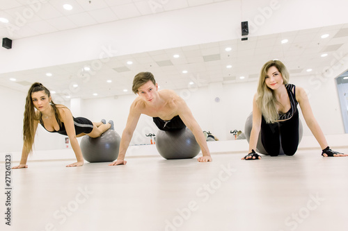Young active people leaning on the floor by stretched arms with legs on ball during workout in gym