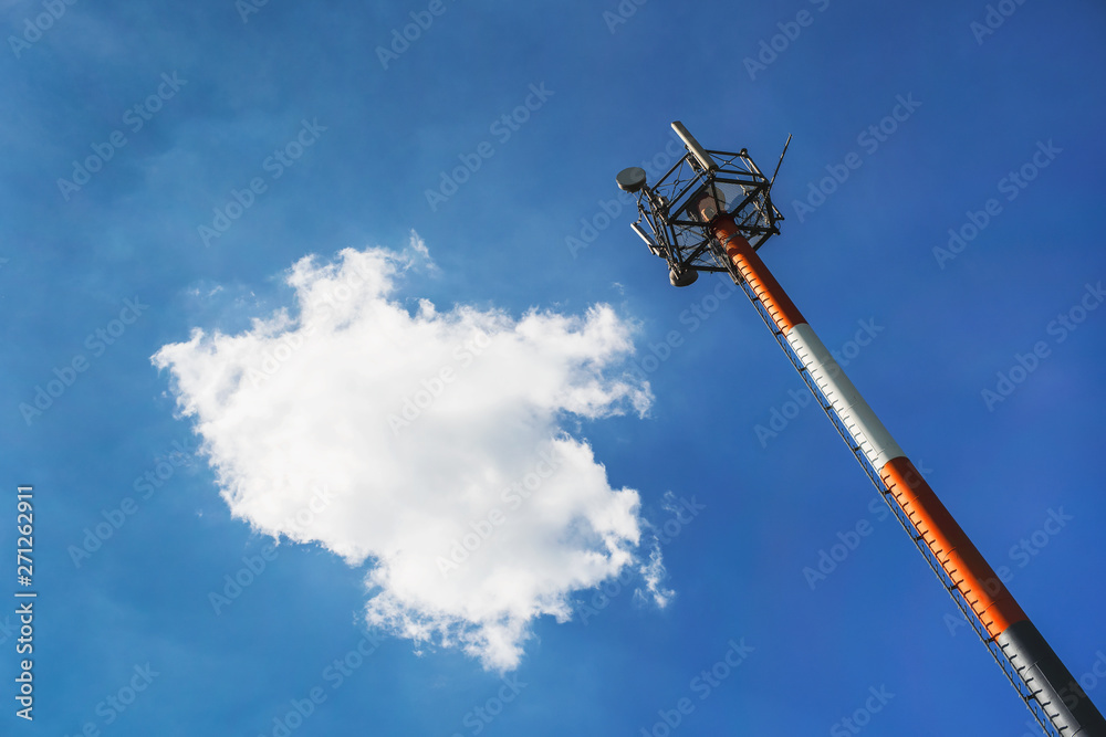red and white mobile wireless radio telecommunication column tower under cloudy clear blue sky