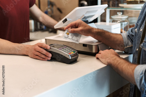 Photo of european man wearing paying debit card in cafe while waiter holding payment terminal
