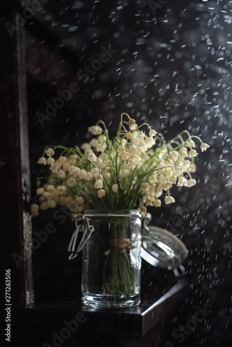 Bouquet of lilies of the valley in small jar with ray of light, dark background, close up