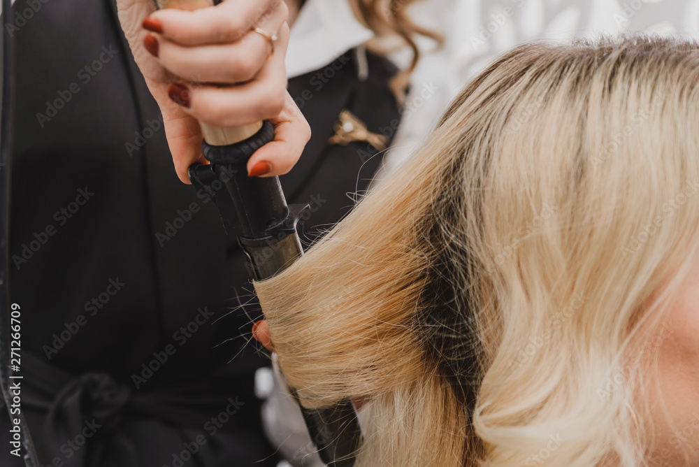 Fototapeta premium Stylist curling hair for young woman. Girl care about her hairstyle. to do curls