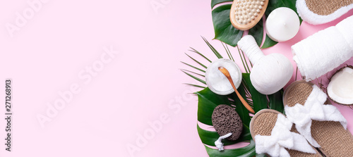 Spa tools: white towel, bamboo slippers, herbal ball, cream, wooden brush, coconut oil, monstera on pink background. Cosmetic products for body treatment. Beauty, relax and massage concept © jchizhe