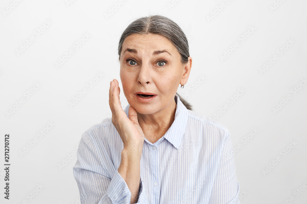 Are you kidding me? Astonished mature elderly woman with wrinkles and gray hair gesturing surprisingly, can’t believe shocking news, big sale, being lost for words, posing at blank copyspace studio