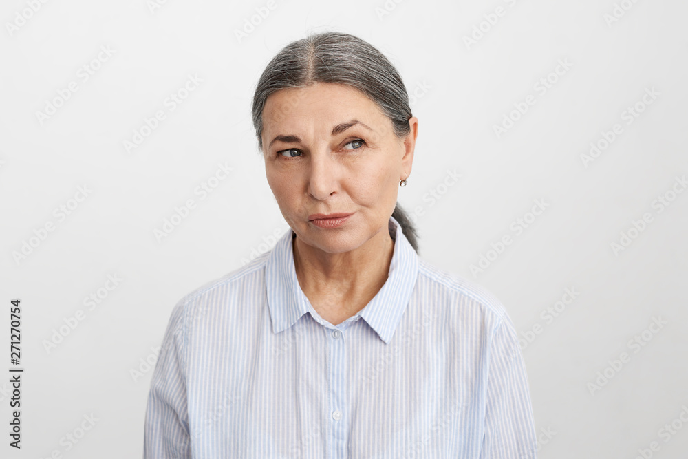Studio portrait of beautiful middle aged European woman with gray hair looking away having doubtful suspicious facial expression, can’t make decision, hesitating, weighing all pros and cons Studio portrait of beautiful middle aged European woman with gray hair looking away having doubtful suspicious facial expression, can’t make decision, hesitating, weighing all pros and cons
