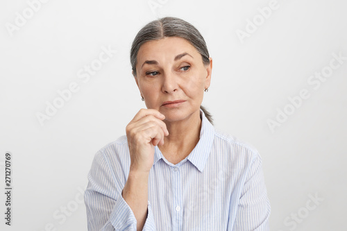 Human facial expressions, feelings and emotions. Sad or thoughtful attractive senior female dressed in striped blue shirt holding hand at her face, having pensive deep in thoughts look, pondering