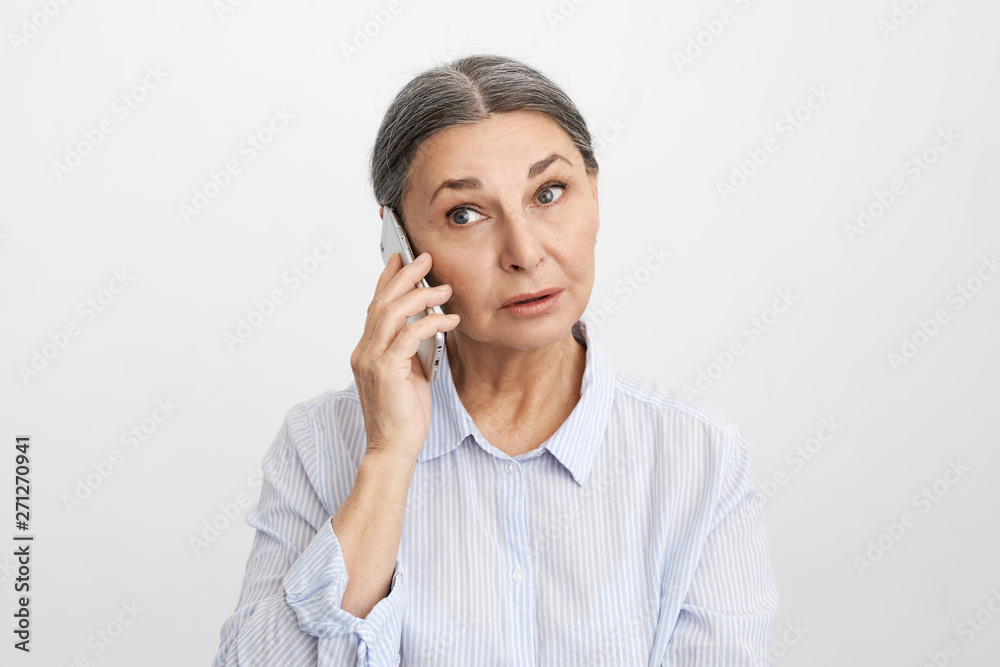 Picture of surprised middle aged mature businesswoman having business talks while speaking to client using mobile. Worried gray haired retired female talking on smart phone with her doctor Picture of surprised middle aged mature businesswoman having business talks while speaking to client using mobile. Worried gray haired retired female talking on smart phone with her doctor