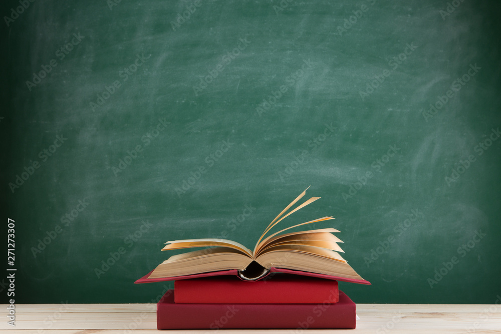 Education and reading concept - group of colorful books on the wooden table in the classroom, blackboard background Education and reading concept - group of colorful books on the wooden table in the classroom, blackboard background