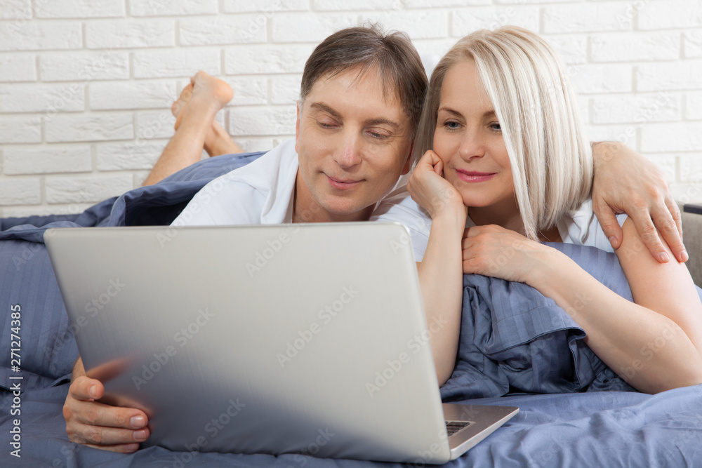 Beautiful amorous couple using laptop, on bed. Beautiful woman and handsome man read the news on internet. Concept relationship. Beautiful amorous couple using laptop, on bed. Beautiful woman and handsome man read the news on internet. Concept relationship.
