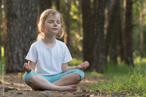 The child is practicing yoga in the forest.